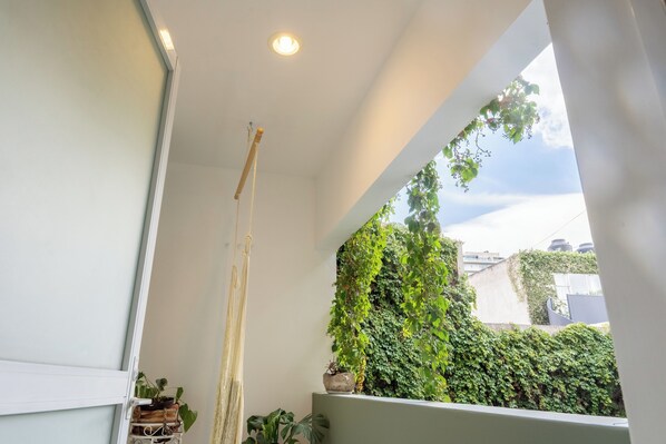 Un balcón con vistas a un muro verde cubierto de hiedra, una planta colgante y una pequeña planta en maceta en el suelo.