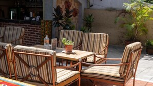 A patio area with striped wicker chairs and a table, surrounded by potted plants and a brick wall. - Monkey Temple Residence (Nagarjun)