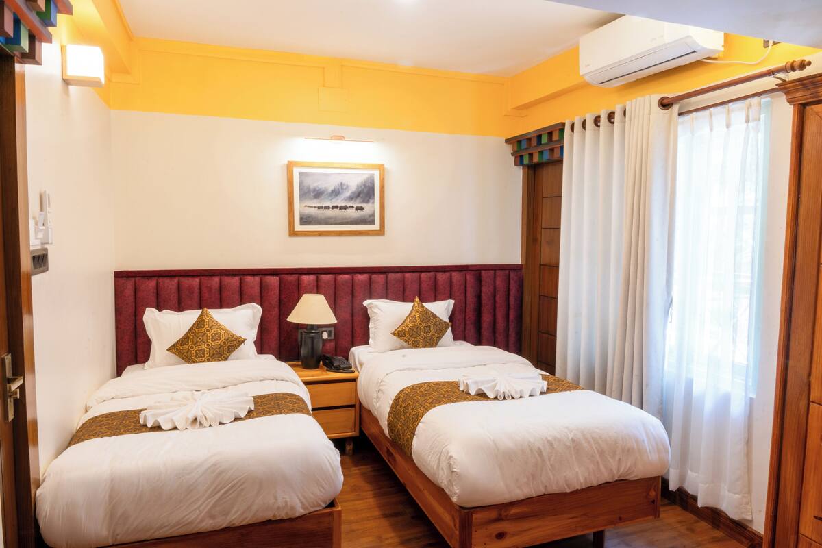 Habitación de hotel con dos camas, un cabecero rojo, un cuadro enmarcado en la pared y una ventana con cortinas.