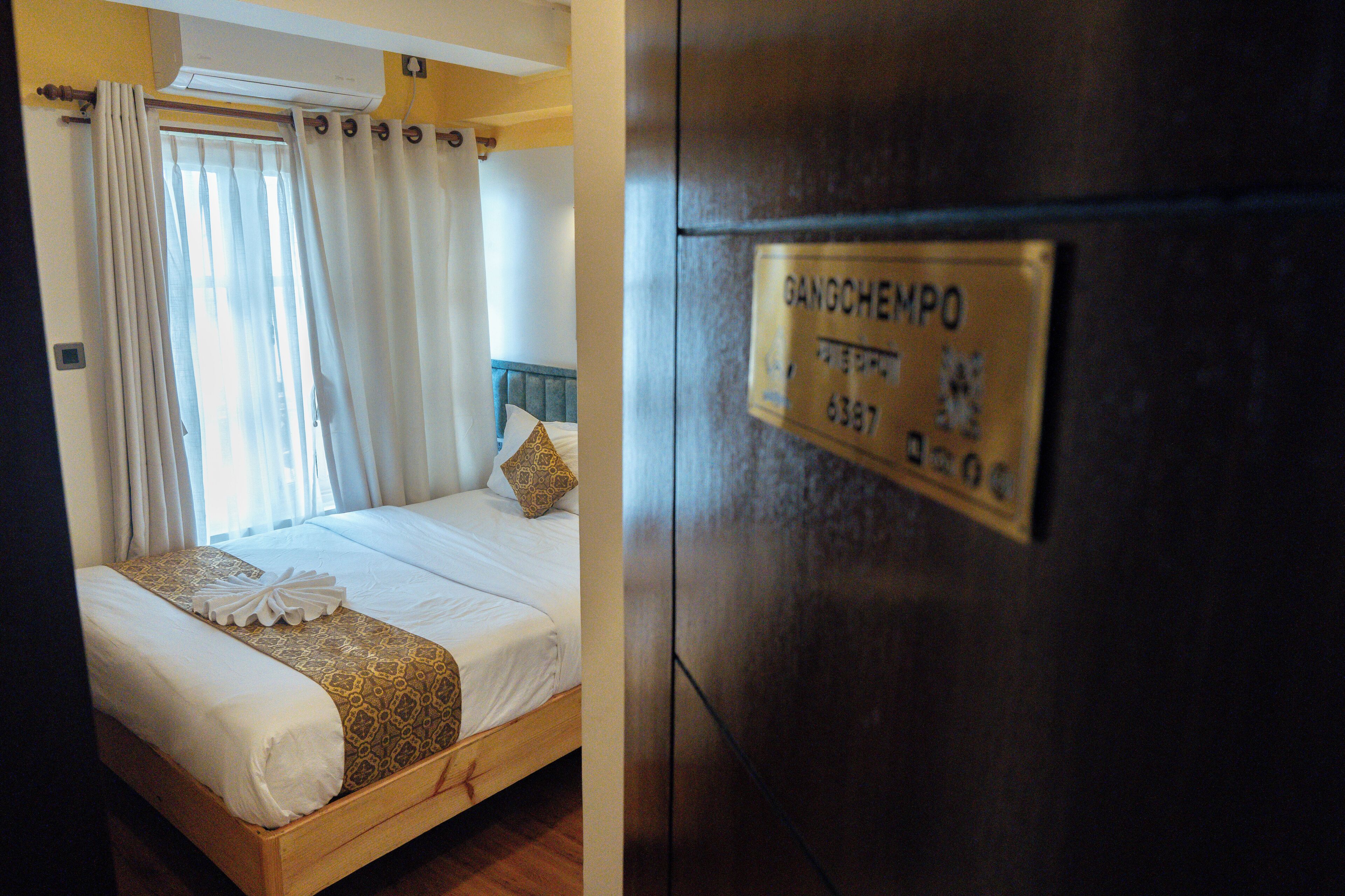 A hotel room with a bed, curtains, a refrigerator, and a sign with text.