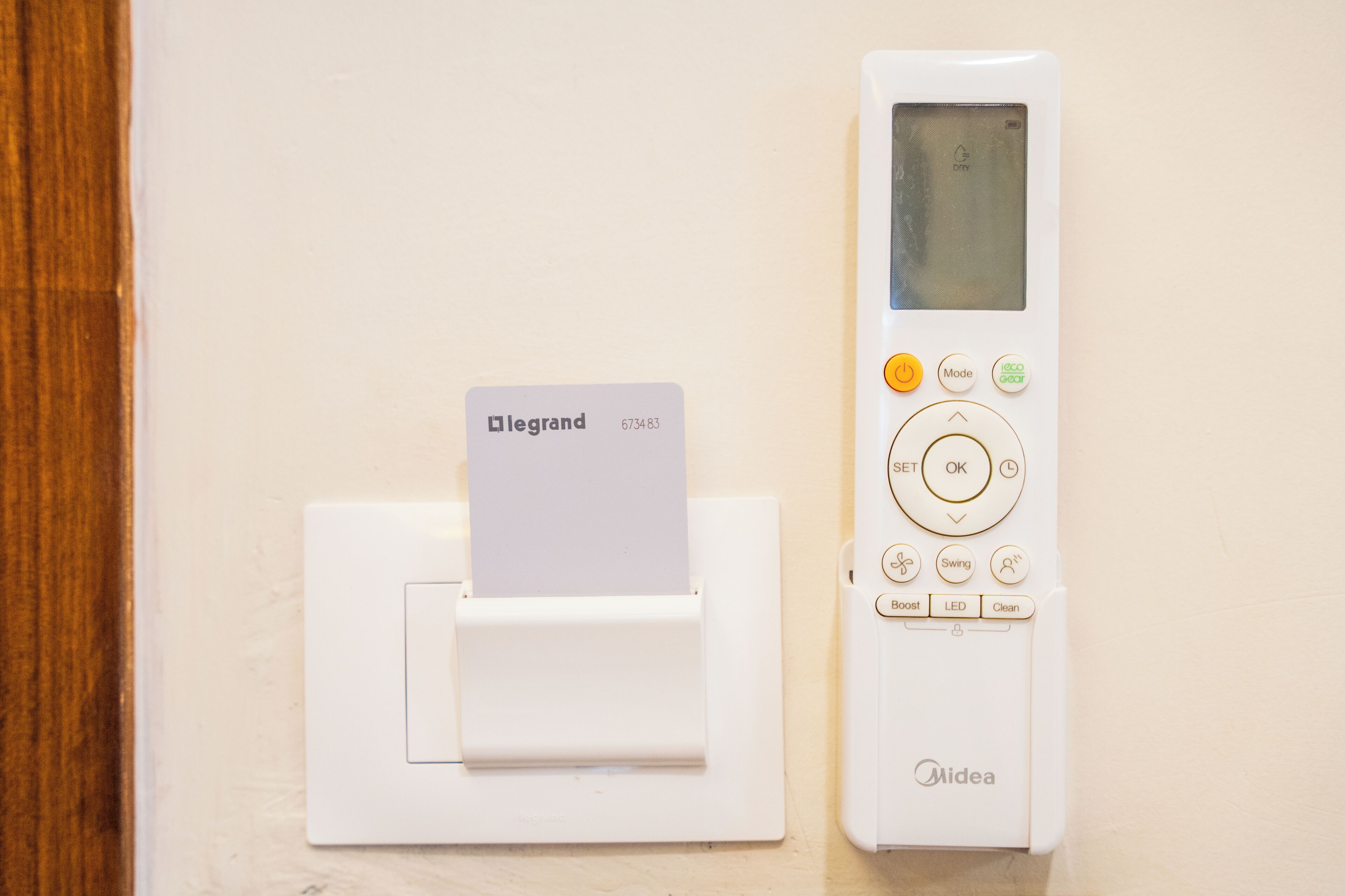 A white Midea thermostat with a card inserted into a slot, and a Legrand card on a wall-mounted device.