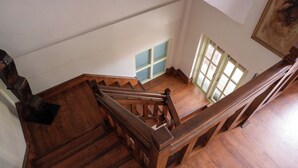 A wooden staircase with a handrail, a small window with blue panes, and a painting on the wall. - Monkey Temple Residence (Nagarjun)