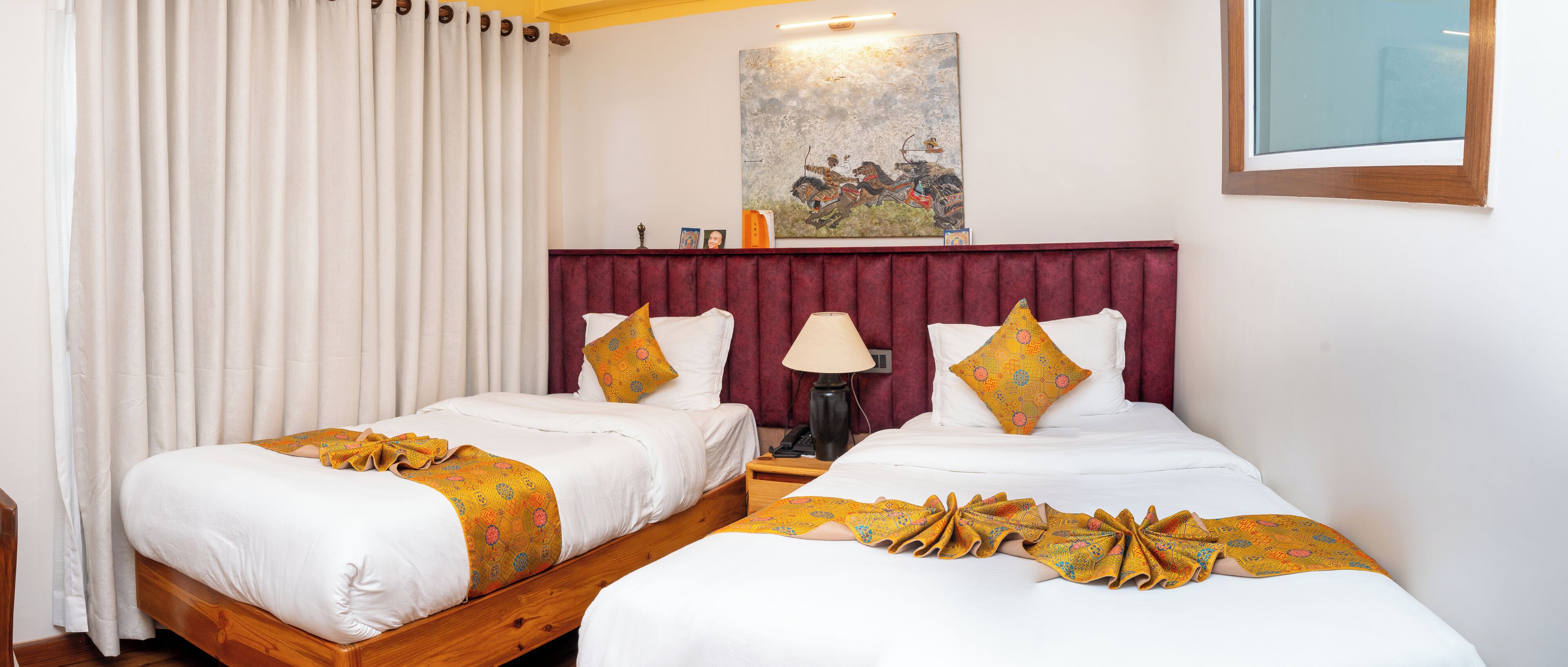 Camera d'albergo con due letti singoli, una testiera in legno, un comodino con una lampada e un quadro appeso al muro.