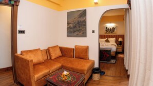 A cozy room with a brown sofa, a small table with a tissue box, a painting on the wall, and a bed with a headboard in the background. - Monkey Temple Residence (Nagarjun)