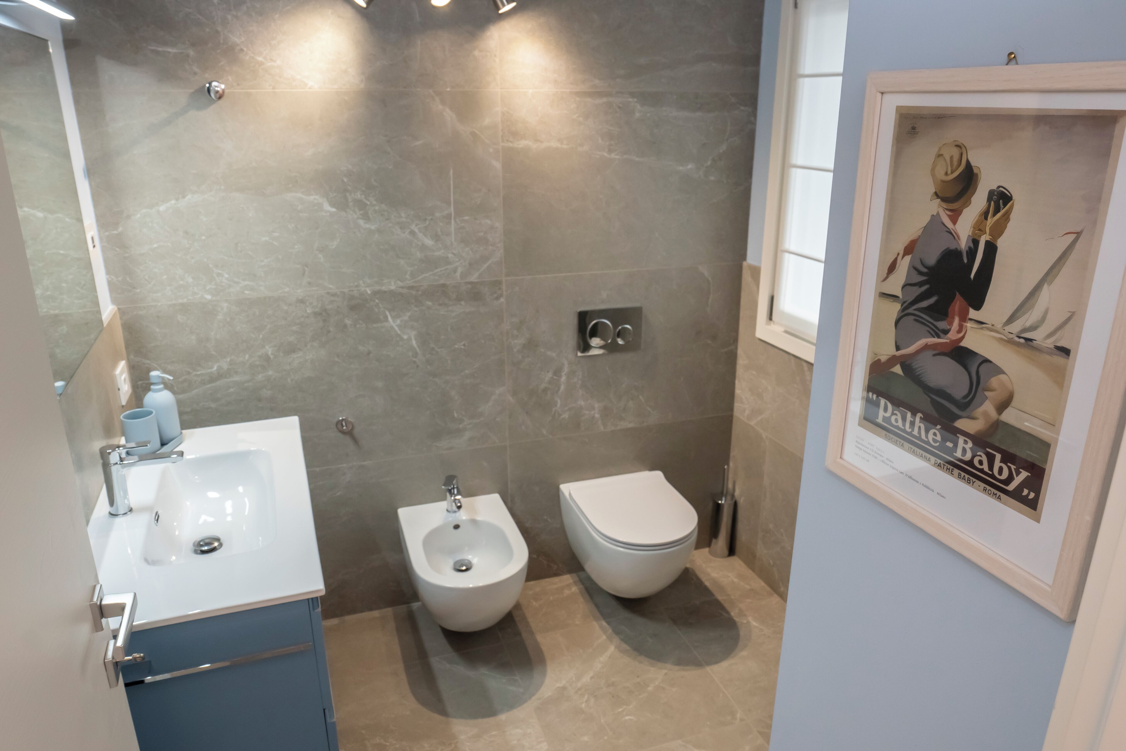 Et moderne badeværelse med bidét, håndvask og toilet. Et billede hænger i en ramme på væggen.
