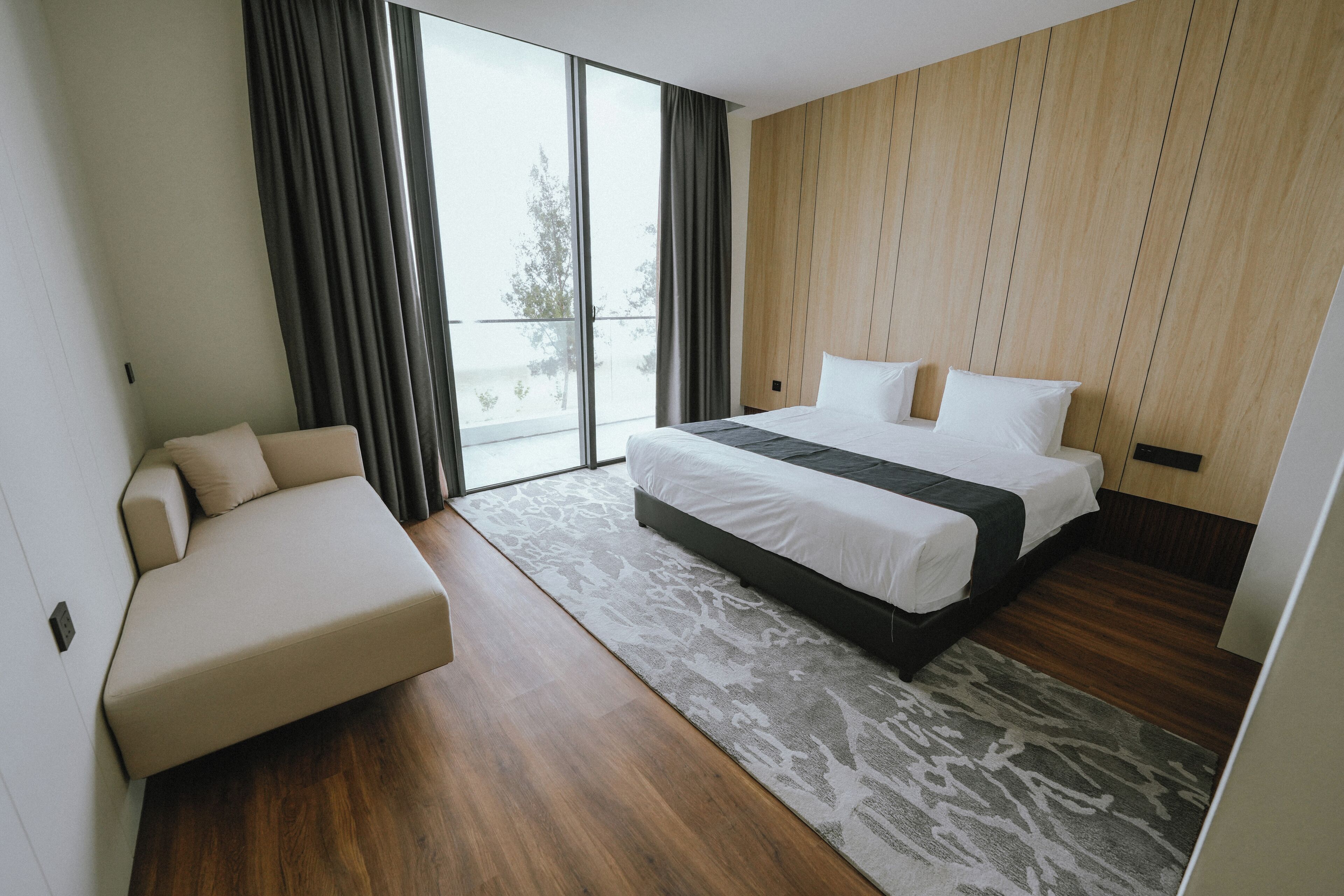 A modern hotel room with a large bed, a sofa, and a view through a sliding glass door.