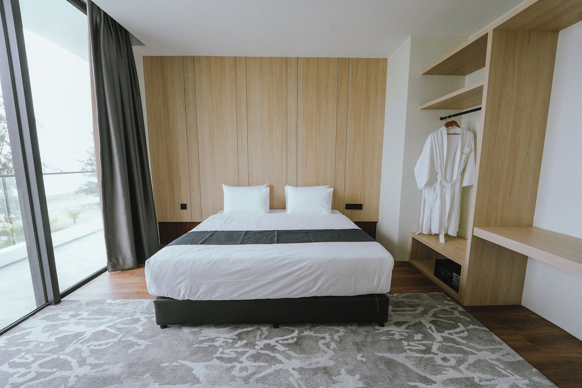 A modern hotel room with a large bed, a wooden wardrobe, and a view through a large window.