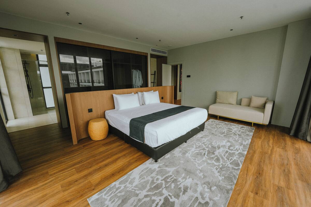 A modern hotel room with a large bed, a sofa, and a wooden floor.