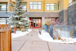 L’entrée d’un hôtel, avec un chemin recouvert de neige, une clôture en bois et un arbre à feuilles persistantes également couvert de neige.