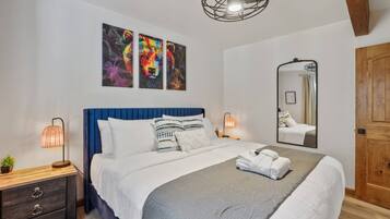 Une chambre à coucher avec un lit, des lampes de chevet, un miroir et des œuvres d’art accrochées au mur.