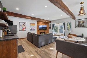 A modern living room with a fireplace, a dining area, and a kitchen with a wooden ceiling.
