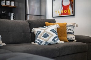 A grey sofa with patterned throw pillows and a framed poster on the wall.