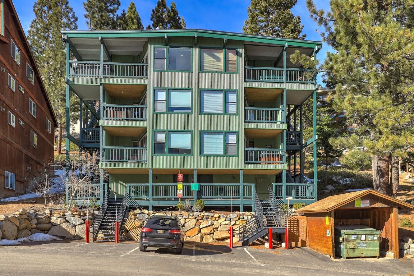 Un immeuble à plusieurs étages doté de balcons, d’un espace de stationnement et d’une petite construction en bois.