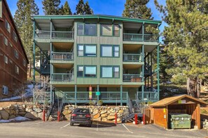 Un immeuble à plusieurs étages doté de balcons, d’un espace de stationnement et d’une petite construction en bois.