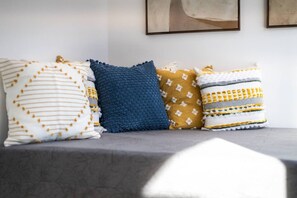 A row of four pillows on a grey sofa against a white wall with abstract art.
