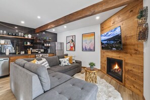 A modern living room with a grey sectional sofa, a fireplace, and a kitchen in the background.