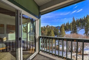 A room with a sliding glass door leading to a balcony with a view of a snowy landscape and trees.
