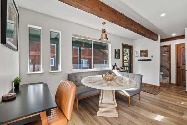 A modern interior with a round dining table, grey upholstered seating, and wooden beams on the ceiling.