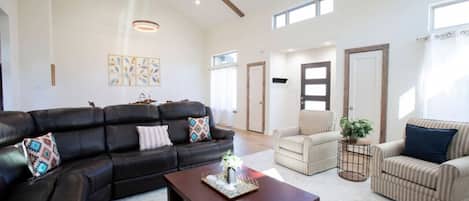 A spacious living room with a black leather sofa, a wooden coffee table, and striped armchairs.