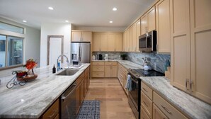 A modern kitchen with wooden cabinets, a stainless steel refrigerator, a microwave, and a marble countertop. - Luxury New Build - 7 Beds! (Bryan)