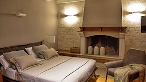 A bedroom with a bed, bedside table, lamp, fireplace, and a chair. - Villa Zita by Villas Guide (Pican)
