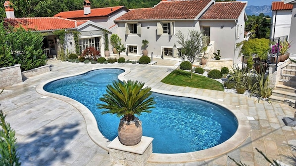 A swimming pool with a curved design, surrounded by a stone patio and a well-maintained lawn.