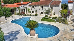 A swimming pool with a curved design, surrounded by a stone patio and a well-maintained lawn.