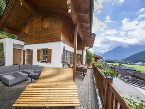 A wooden chalet with a balcony, outdoor seating, and a view of the countryside.