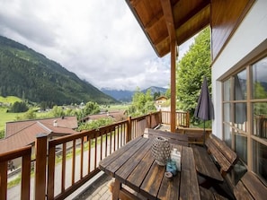 A wooden deck with a table and benches overlooking a valley with houses and mountains.