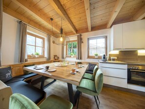 Eine gemütliche Küche mit Holzbalken, einem Esstisch mit Stühlen und einem modernen Backofen.