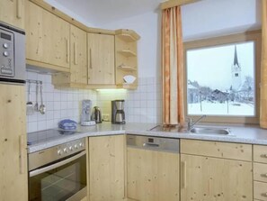 Una cocina con armarios de madera, una estufa, un fregadero y una ventana con vistas a la aguja de una iglesia.