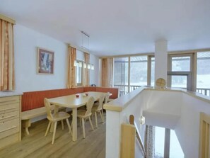 A dining area with a wooden table and chairs, a bench, and a view of the outdoors through large windows.
