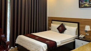 A hotel room with a bed, a nightstand, a desk, a chair, and a painting on the wall. - Hoang Lan Hotel KDT Xala HN - BAY LUXURY (Hanoi)