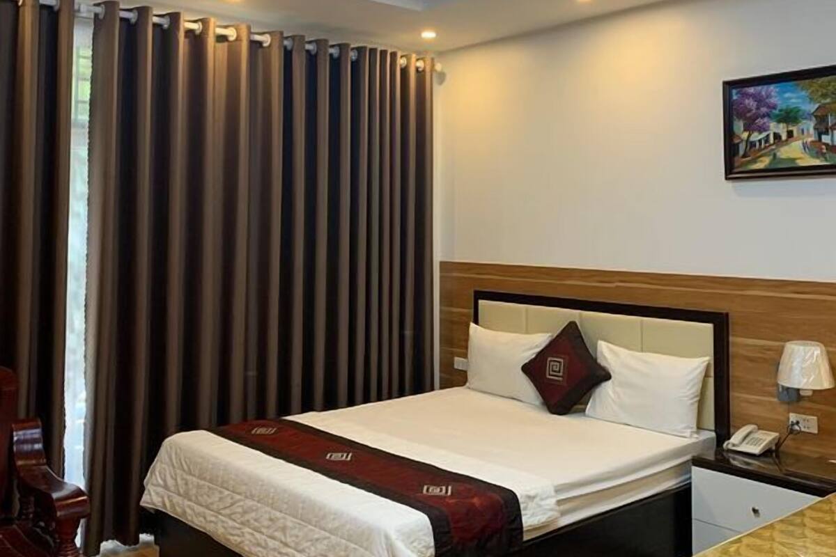 A hotel room with a bed, a nightstand, a desk, a chair, and a painting on the wall.
