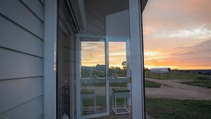 A glass door leading to a porch with a view of a sunset over a rural landscape.