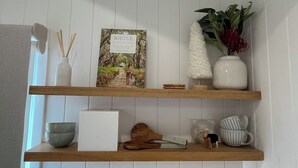 A shelf with a book titled 'WHOLE by Natural Daddy', a vase with red flowers, a bowl, a white box, and a wooden spoon.