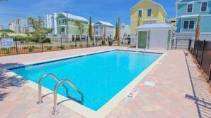 Una piscina con una escalera de metal, rodeada por un camino de ladrillo y una valla.