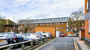 Un parking où les voitures sont rangées en rangées, un bâtiment en briques avec de nombreuses fenêtres et un ciel dégagé.
