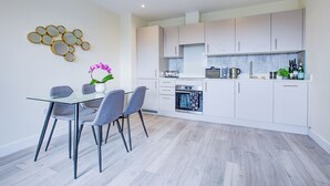 Une cuisine moderne avec des meubles blancs, un four encastré et un coin repas comprenant une table et des chaises en verre.