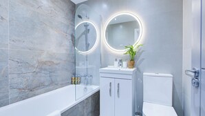 A modern bathroom with a glass-enclosed shower, a white bathtub, a toilet, and a vanity with a mirror.