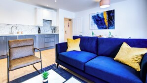 A modern living room with a blue sofa, a brown chair, and a small table with a plant. - Hybrid Resi - New Malden | 3 Bed Apartment (New Malden)