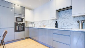 A modern kitchen with built-in appliances, marble backsplash, and light-colored cabinetry. - Hybrid Resi - New Malden | 3 Bed Apartment (New Malden)