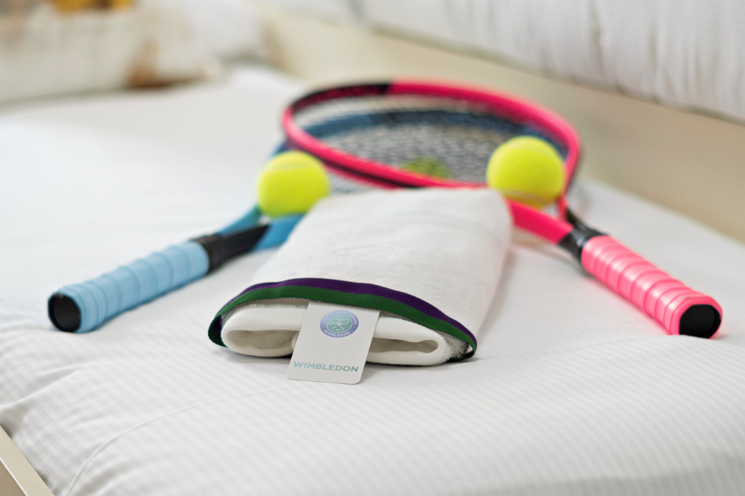 A tennis racket, two tennis balls, and a tennis bag on a bed.