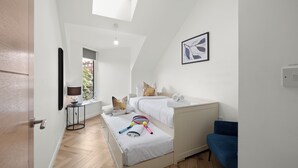 A bedroom with a skylight, two beds, a bedside table with a lamp, a blue chair, and a tennis racket on the bed. - Hybrid Resi - Mitcham | 2 Bed Apartment (Mitcham)