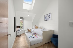 A bedroom with a skylight, two beds, a bedside table with a lamp, a blue chair, and a tennis racket on the bed.