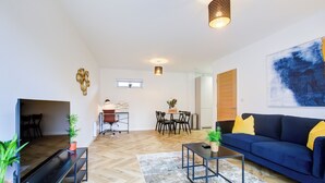 A modern living room with a blue sofa, a coffee table, a dining area with chairs, and a large abstract painting on the wall. - Hybrid Resi - Mitcham | 2 Bed Apartment (Mitcham)