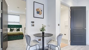Una habitación moderna con una cama, una mesa redonda con dos sillas, una planta en maceta y una obra de arte enmarcada en la pared.