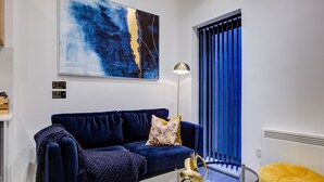 Una sala de estar moderna con un sofá azul oscuro, una mesa de centro de vidrio y un cuadro abstracto grande en la pared.
