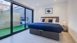A modern bedroom with a large bed, a sliding glass door leading to a balcony, and a framed artwork on the wall. - Hybrid Resi - Fulham | 2 Bed Apartment (London)