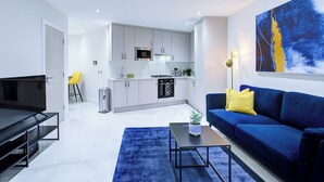A modern living room with a blue sofa, a coffee table, and a TV. - Hybrid Resi - Uxbridge|1 Bed Apartment (Uxbridge)